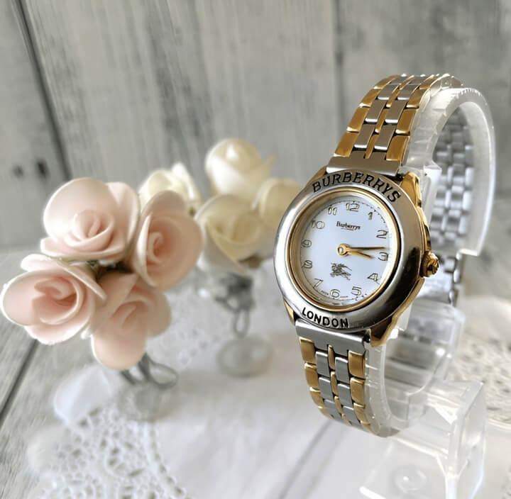 นาฬิกา Burberry ผู้หญิงสีทองวางอยู่บนผ้าปูโต๊ะสีขาว พร้อมช่อกุหลาบขาวจัดวางอย่างประณีต เพิ่มความหรูหราและมีเสน่ห์